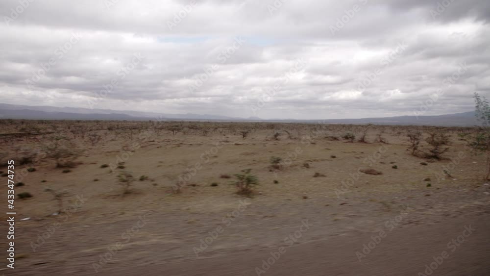 A view of a wide savanna road in Kenya, with many trucks driving along it. The weather is cloudy, yet it is still bright. The mountains are covered in thick shrubbery and tall grass. A view of a wide savanna road in Kenya, with many trucks driving along it. The weather is cloudy, yet it is still bright. The mountains are covered in thick shrubbery and tall grass.