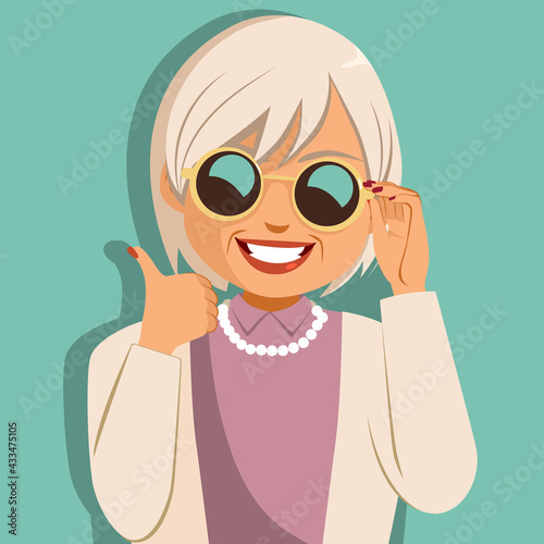 Funny cheerful old woman holding sunglasses making thumbs up hand gesture