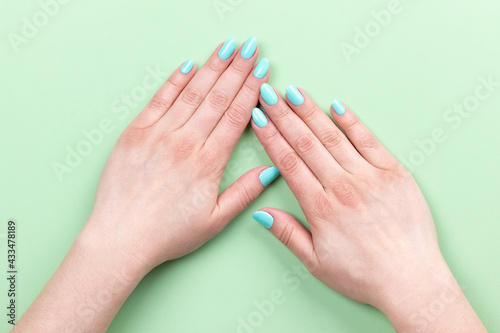 Female hands with beautiful manicure - mint blue nails on green background