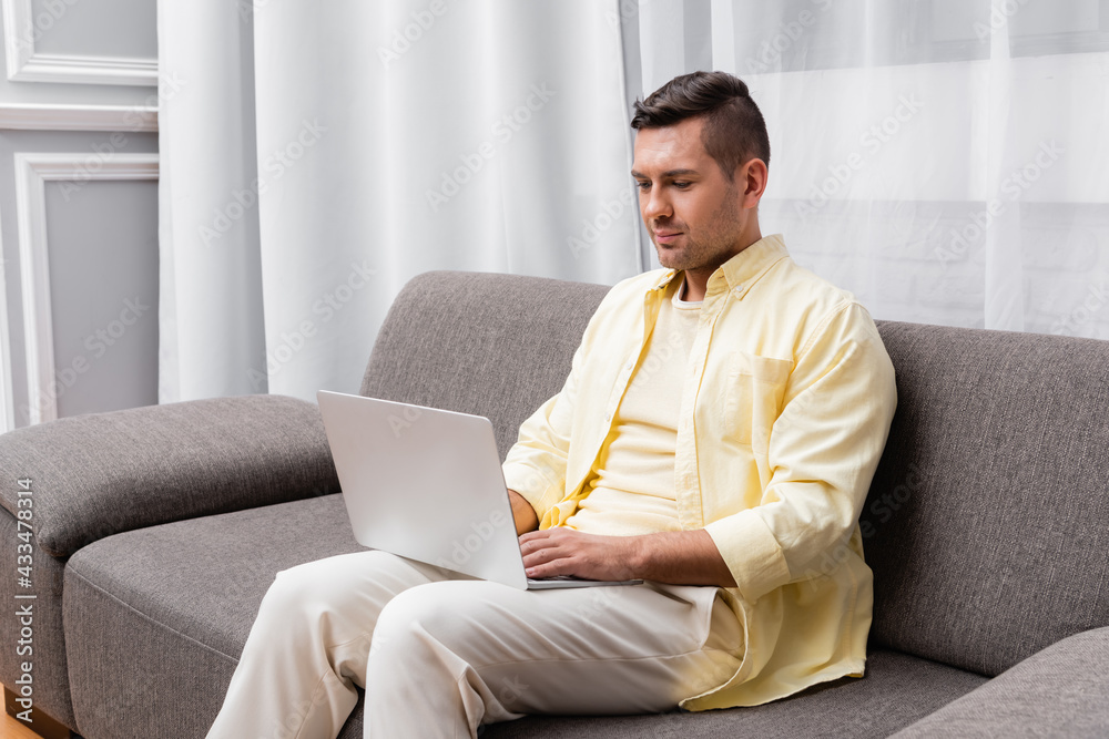 young freelancer in casual clothes sitting on couch with laptop young freelancer in casual clothes sitting on couch with laptop