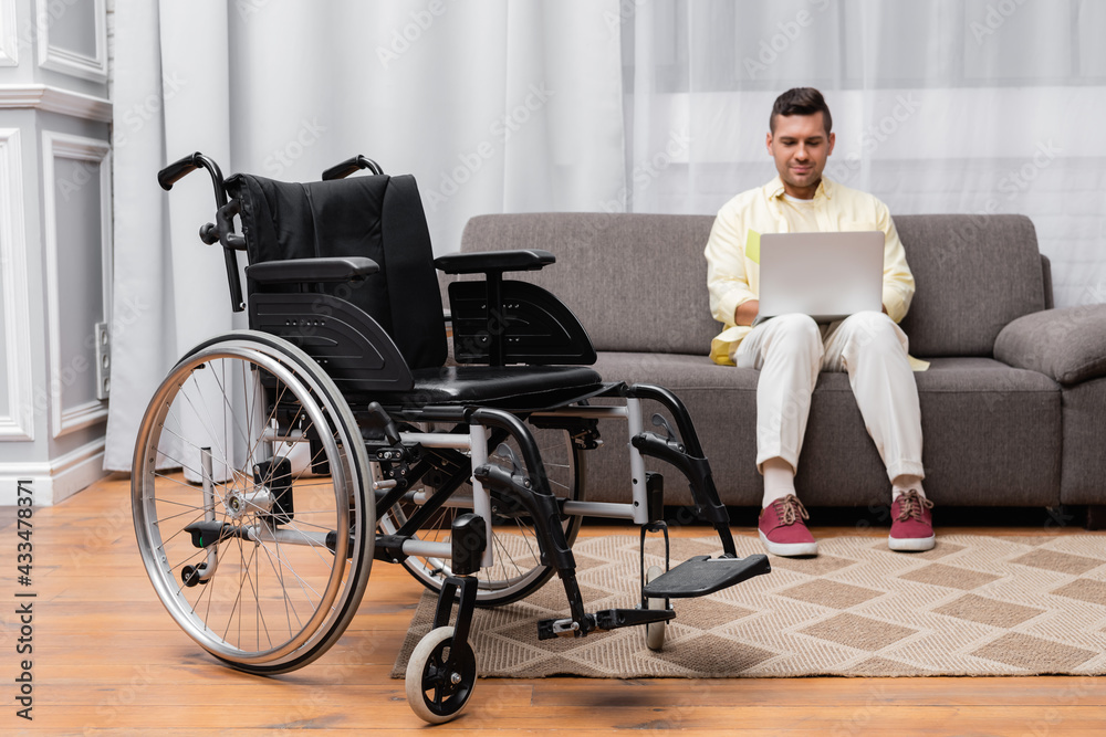 disabled man working on sofa with laptop near wheelchair on foreground disabled man working on sofa with laptop near wheelchair on foreground