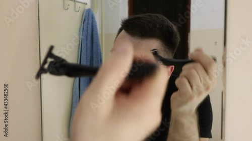 A man in the bathroom shaves the outline of his hair in front of the mirror. Leveling haircuts, shaving the head.