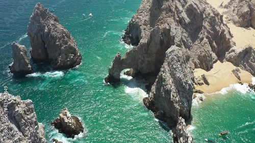 Aerial view of the Arch of Cabo San Lucas with some waves crashing in the rock, the drone slowly rotating.