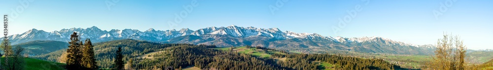 Extra wide panorama of the Tatra Mountains with trees, forests and meadows in Podhale region in Poland. Early morning in spring, sunrise light