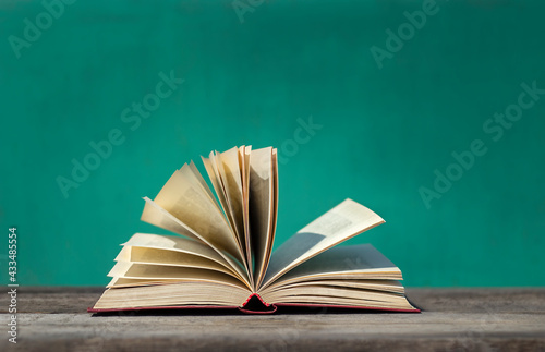 open book with flying pages close-up lies on a wooden surface on a green background