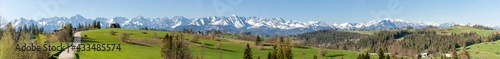 Wide panorama of the Tatra Mountains in spring, with a village paved road, highlander houses, forests and green grass pasture