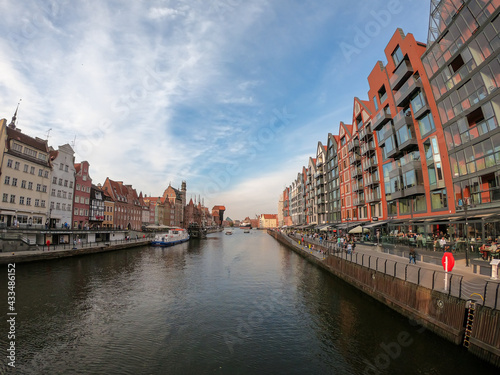 A panoramic view on the shores of Martwa Wisla flowing through Gdansk in Poland, with medieval port crane. New architecture meeting with medieval constructions. Sunny day. Calm water. City tour