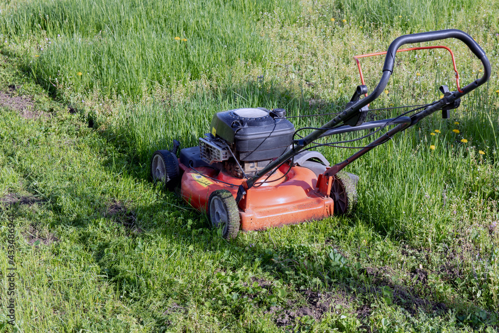 Obraz premium An old gasoline lawn mower mows the lawn. Side view.