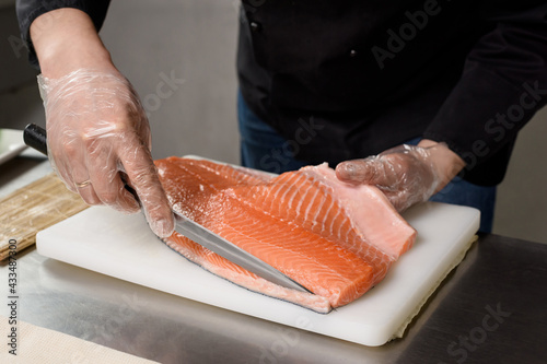 The process of preparing delicious fish dishes. Japanese restaurant cuisine. The sushi chef holds a knife in his hand and cuts off a slice of fresh salmon fillet. Ingredients for making sushi rolls.