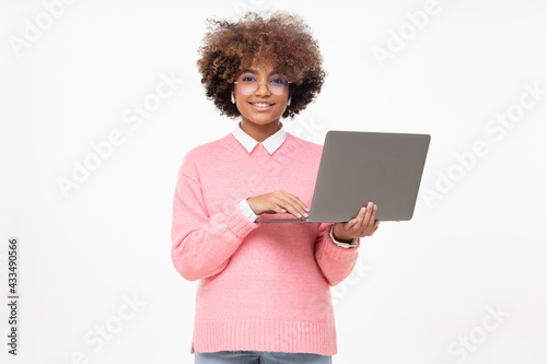 Smiling african american teen girl, high school or online course student holding laptop and looking at camera, isolated on gray background © Damir Khabirov