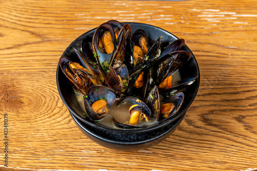 Black bowl with steamed mussels in their juice on wooden table