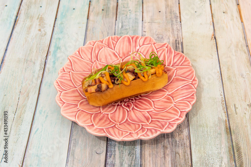 Brioche shaped like a hot dog stuffed with Galician cooked octopus on a plate shaped like a pink flower photo