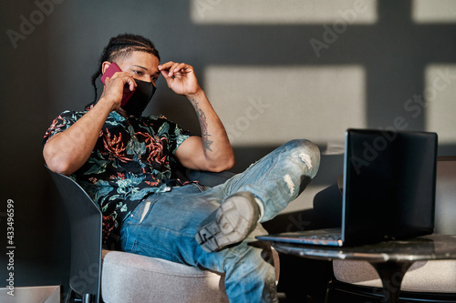 young latin man working with his laptop from home and talking on his cell phone