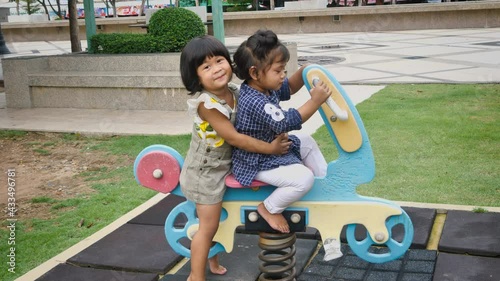 Two happy asian kids adorable are playing at the playground, kids having fun playing with rocking horse and hugging, activities kids, enjoy outdoor in summer time.