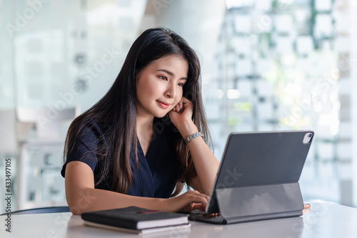 Front view of a beautiful woman sitting and working with a tablet at the office.