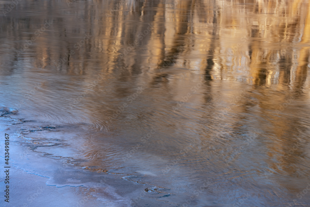 Obraz premium Winter landscape at sunrise of the Kalamazoo River with ice formation and reflections of trees in calm water, Michigan, USA