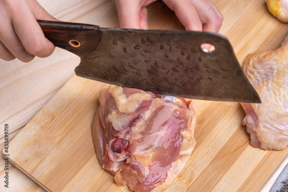 Female hands cut a chicken thigh with a chef's cleaver