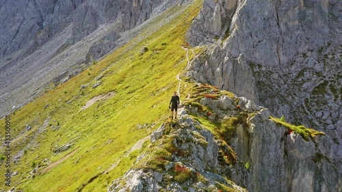 Young man on top of a mountain peak. Aerial drone shot surrounding him
