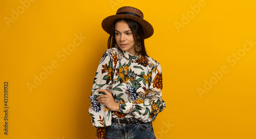 beautiful attractive stylish brunette woman posing isolated on yellow studio background in trendy fashion clothes outfit, printed blouse and hat, smiling happy, accessories