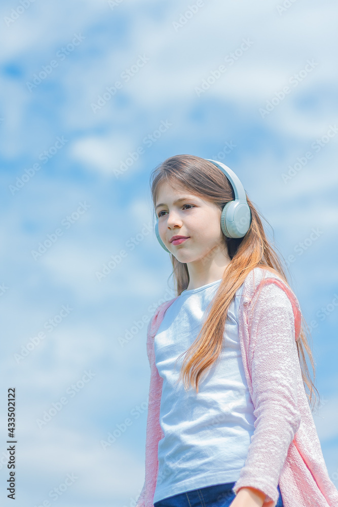 Girl child wearing headphones outdoors. girl in headphones stands against the background of the cloudy sky. Girl child wearing headphones outdoors. girl in headphones stands against the background of the cloudy sky.