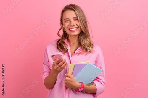 blond pretty woman in pink shirt smiling holding holding notebooks and using smartphone