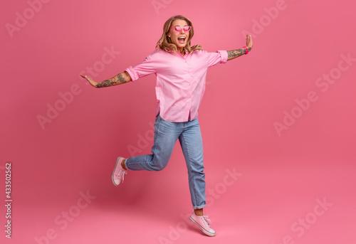 blond pretty woman in pink shirt and jeans smiling jumping