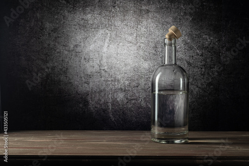 A bottle with a strong drink, on a wooden table top, on a background with a stain