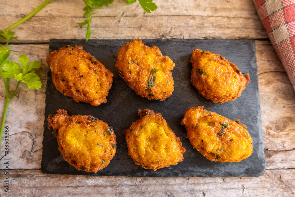 salty fritters with parsley, served on a slate plate and a rustic wood background. salty fritters with parsley, served on a slate plate and a rustic wood background.