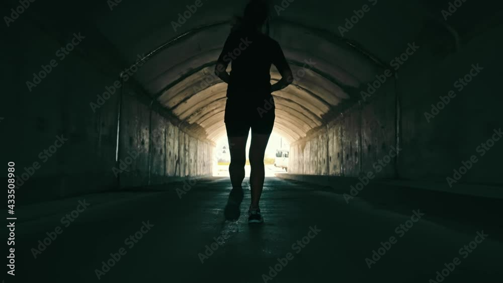 woman running in a dark tunnel to meet the light. Silhouette of a woman from behind running to the light.