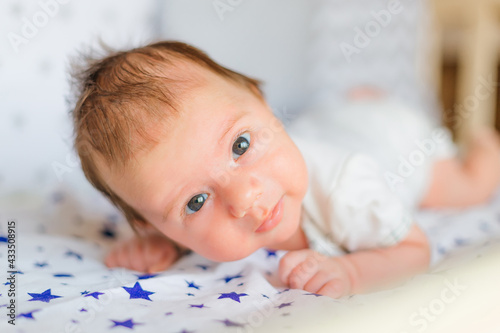Adorable baby boy in white bedroom. Newborn child relaxing in bed. Nursery for young children.