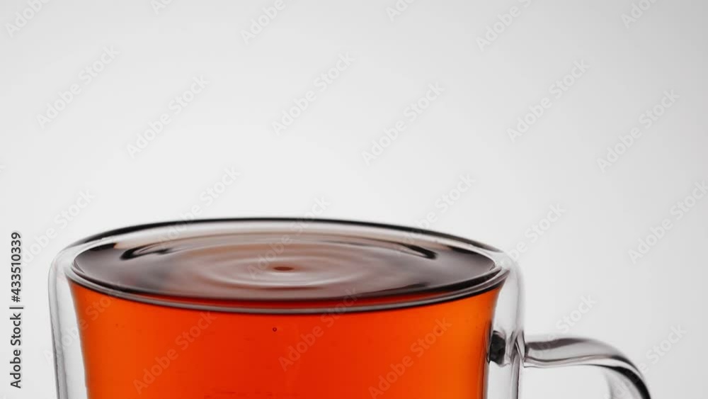 A drop of tea drips into a full glass tea mug
