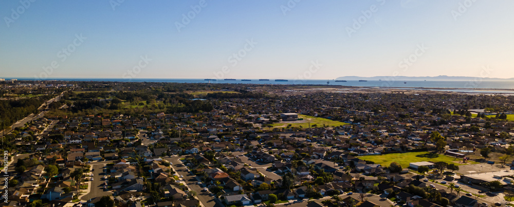 Aerial view of a coastal suburban neighborhood with the ocean and mountains and ships lined up on the ocean.