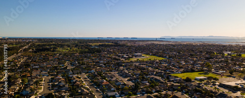 Aerial view of a coastal suburban neighborhood with the ocean and mountains and ships lined up on the ocean. © Images By Chaos