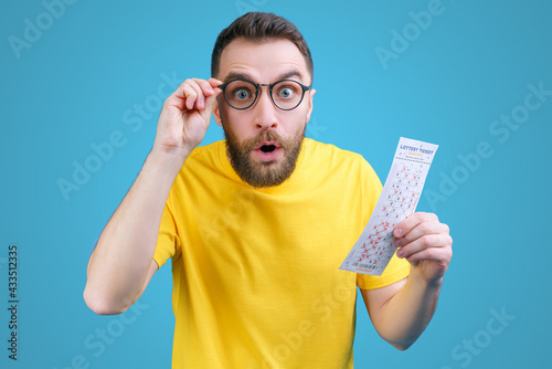 Man holding lottery ticket in hands with astonished face expression, unable to believe in his victory