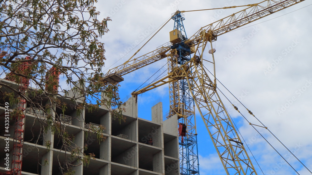 The frame of a building under construction and a crane on the background of a blue cloudy sky. The frame of a building under construction and a crane on the background of a blue cloudy sky.