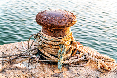 An old and rusted bollard, with several ropes rolled up on itself.
