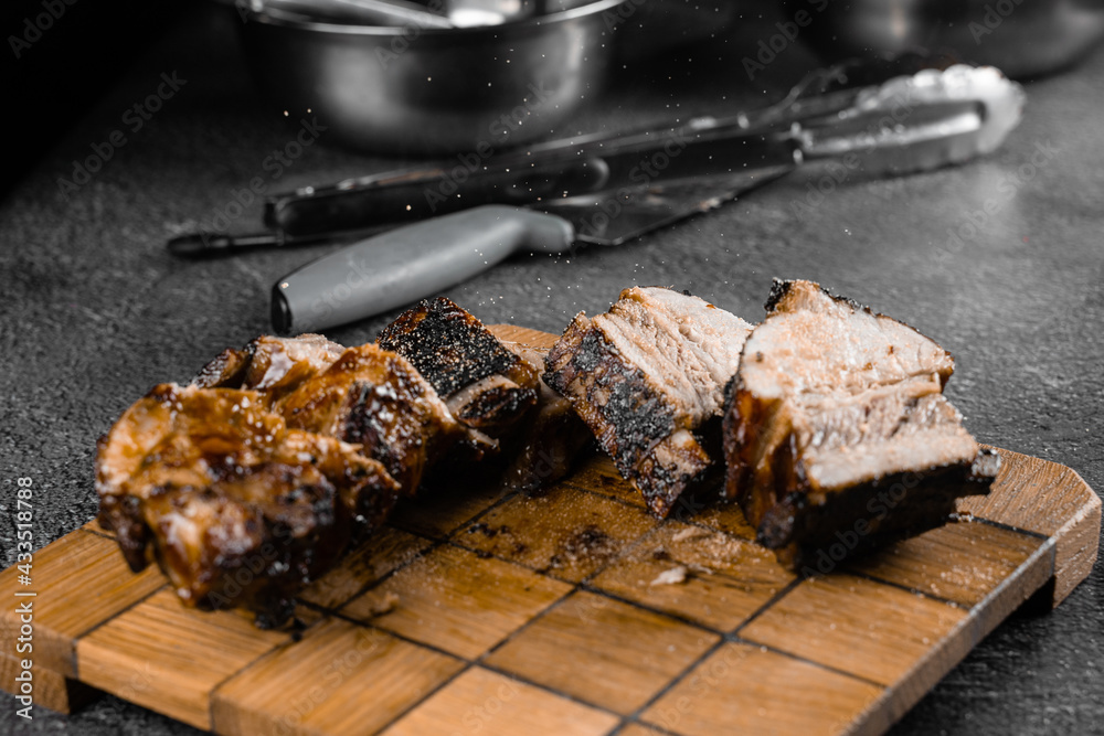 Grilled ribs slicing on a wooden plate on a gray background. Barbecue decoration.