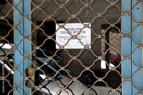 Closed Shop with sign due to discontinuation of activity ' during pandemic Covid-19 in Italy..Text wtitten in Italian language with thanks to customers. Italy. photo