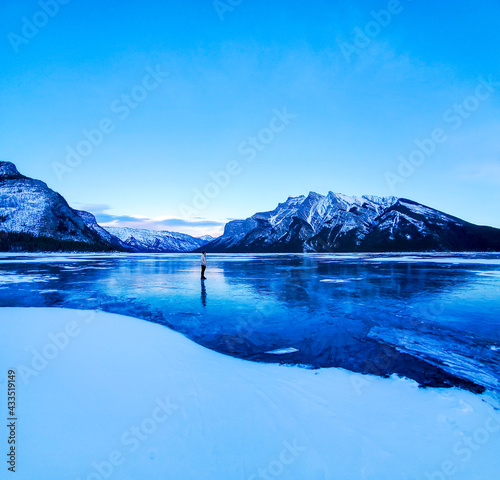 Man Standing In The Middle Of A Frozen Lake Surrounded By Mountains