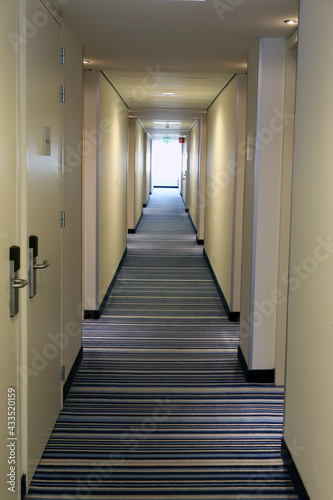 Long hotel corridor with doors. Carpets on the floor  sunlight at the end in background.