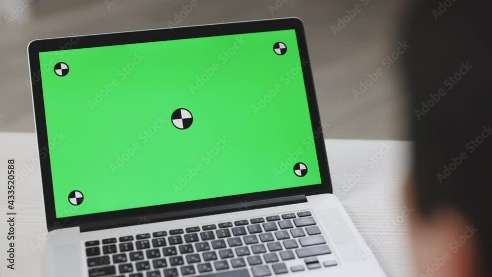 Back view of businessman look green screen laptop in office. Close up shot of modern chroma key green screen laptop computer set up for work on desk at day - remote work, technology concept