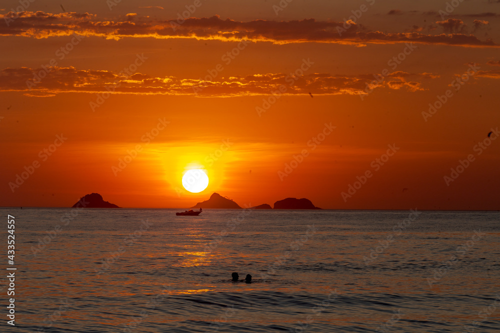 Pessoas assistem, dentro do mar, pôr do sol na Praia de Ipanema, Rio de Janeiro, Brasil