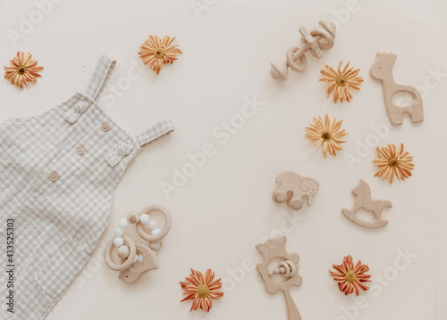 Light soft baby pants with wooden toys and flowers. Fashion newborn, bohemian style, neutral beige colors. Flat lay, top view. Natural textile, pastel background.