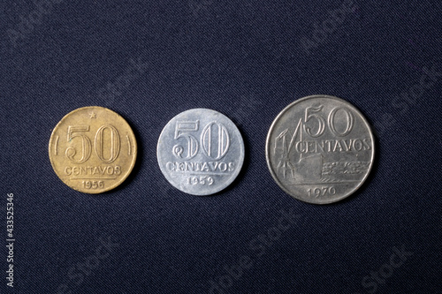 Three coins with a value of fifty cents dated 1956, 1959 and 1970 respectively positioned in ascending order of year used in Brazil. They are on a dark black background. photo