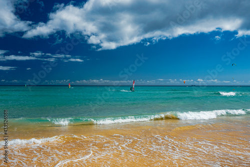 Beautiful turquoise water beach, blue crystal clear water with waves, windsurfers, surfers, cloudy expressive deep blue sky, emerald coast, atlantic ocean