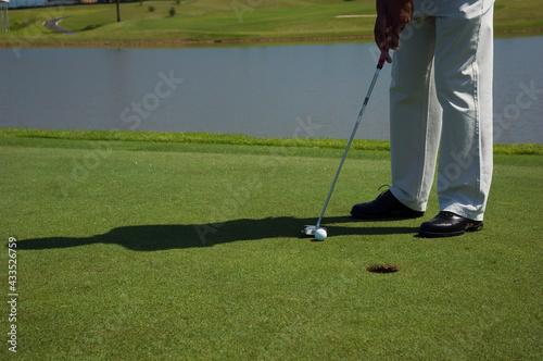 Detalhe de taco de golf, as pernas do golfista e a bola, gramado e o buraco. Esporte ao ar livre.