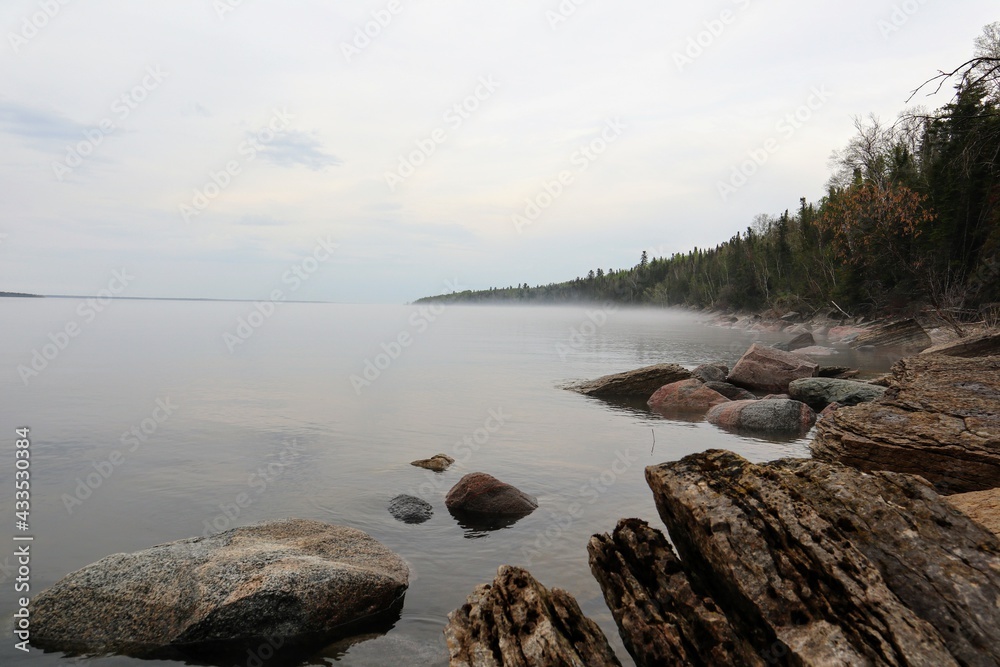 Fog on a calm lake with a rocky shore.