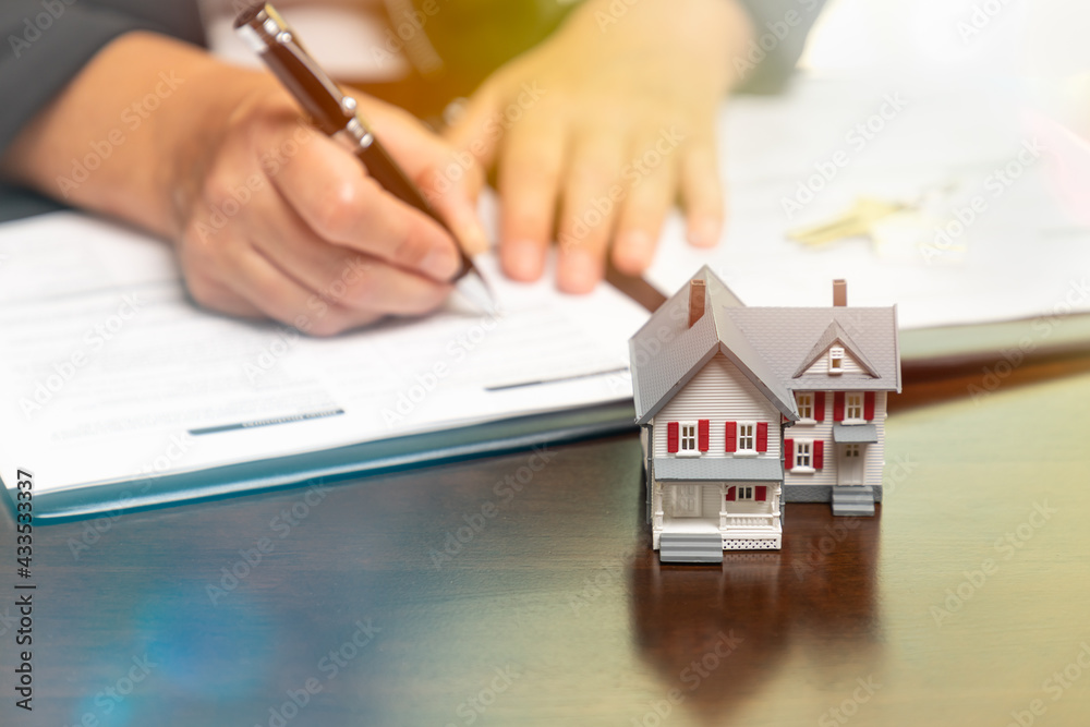 Fototapeta premium Man signing real estate contract papers with small model home in front.