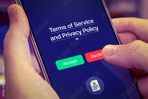 Smartphone user refuses to accept Terms of Service and Privacy Policy mobile app. Dark app interface with Accept and Decline buttons. Finger touches the Decline button photo