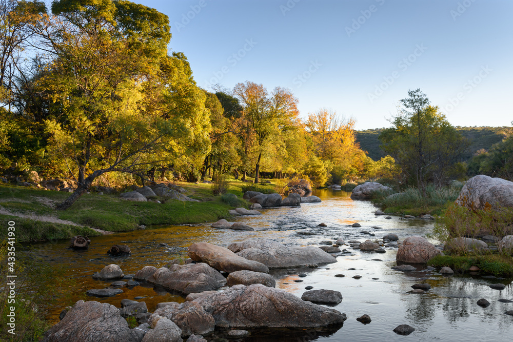 Tarde de otoño en el río Cosquín con follaje naranja y verde Tarde de otoño en el río Cosquín con follaje naranja y verde